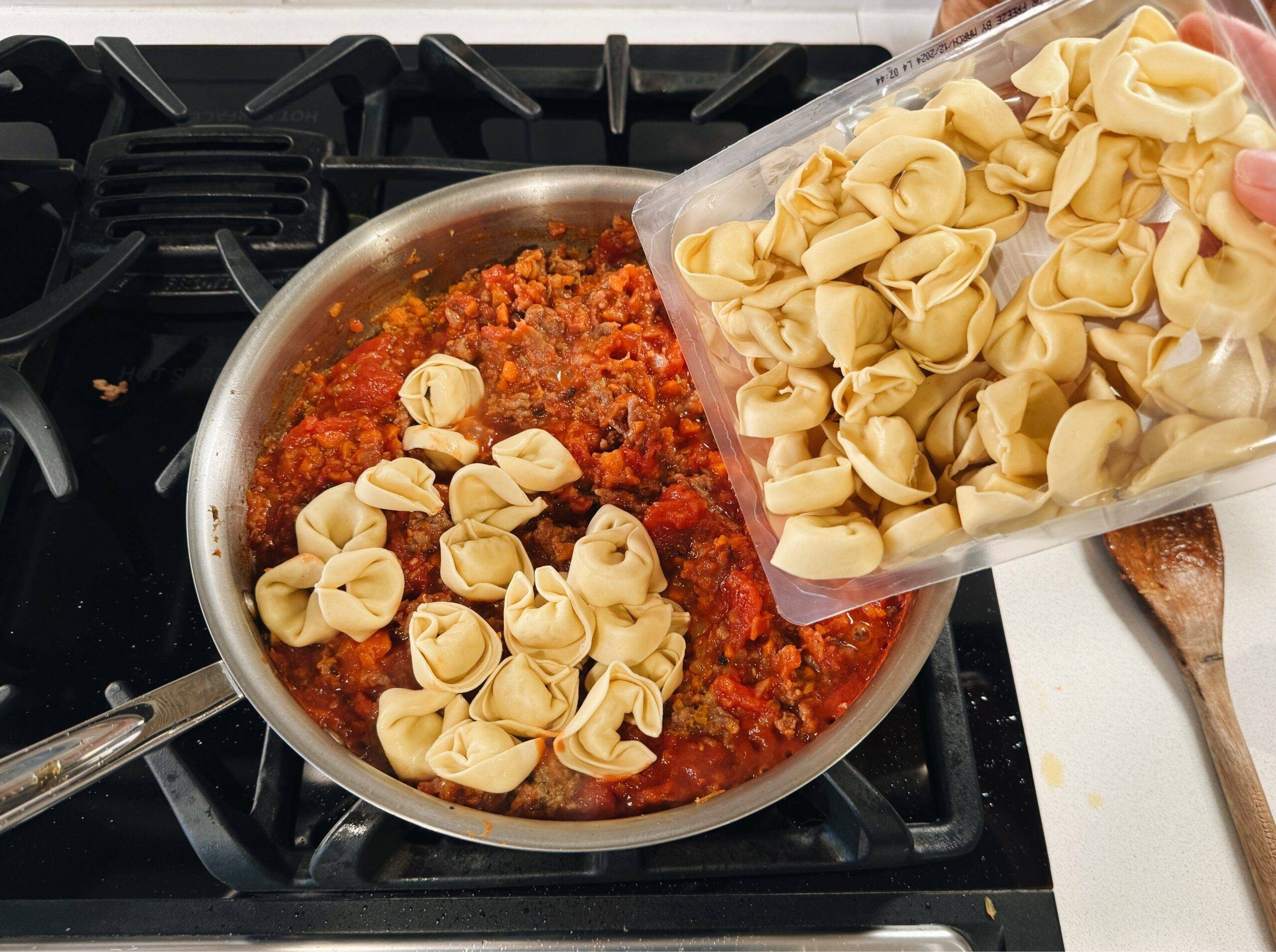 Adding sauce and tortellini to pan.