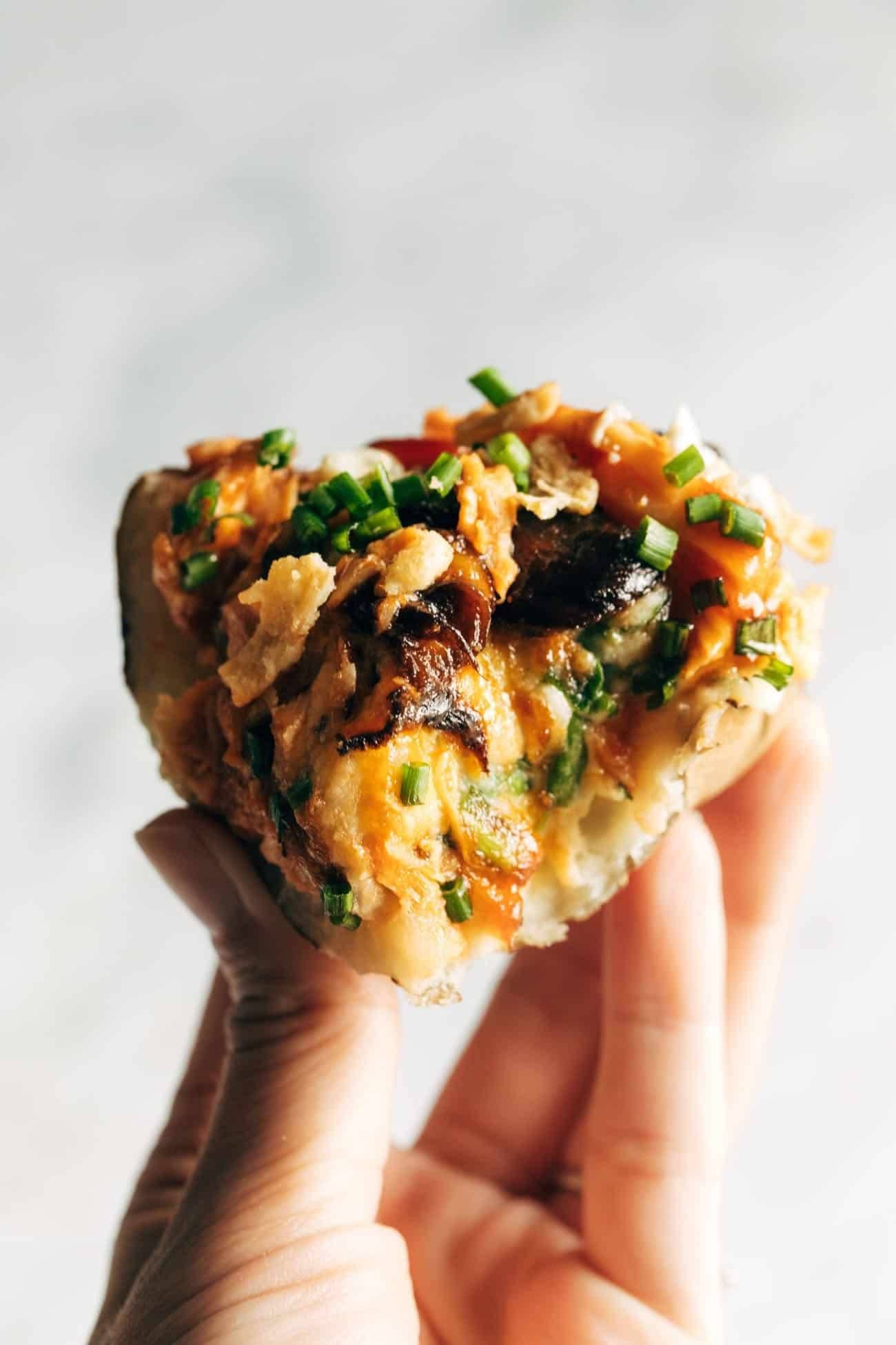 White hand holding a loaded BBQ baked potato with a bite out of it. 