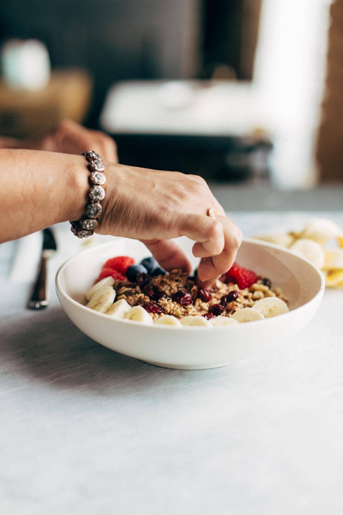 Hands styling a bowl of granola and fruit to take a photo.