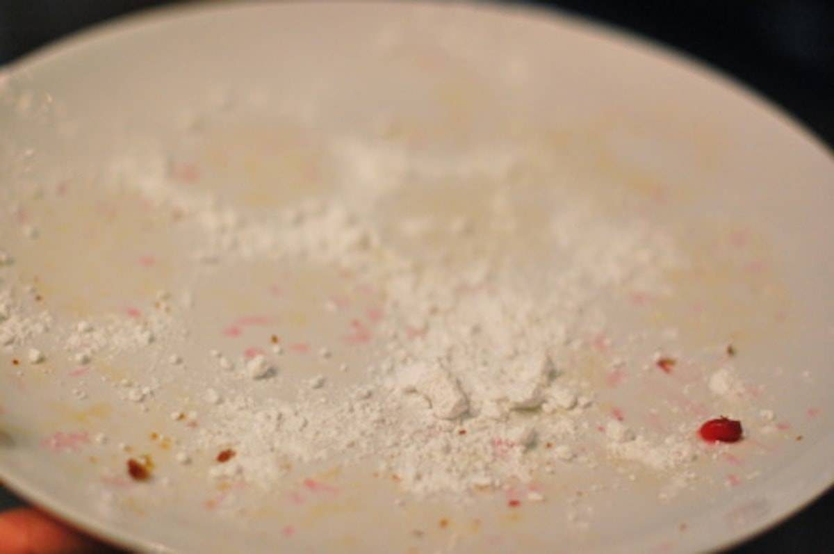 White plate with muffin remains including pomegranate seeds and powdered sugar.