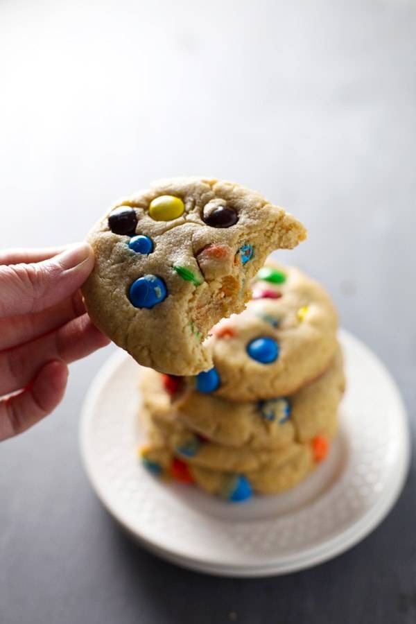 Big soft M&M cookies on a stack of white plates.