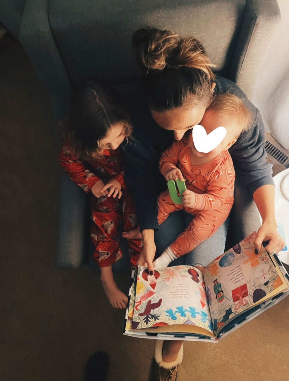 White woman reading a book to her two daughters in a chair.