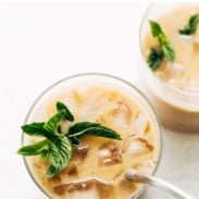 Clear glass with ice cubes, creamy vanilla coffee, and a fresh bundle of mint floating atop next to a silver spoon.